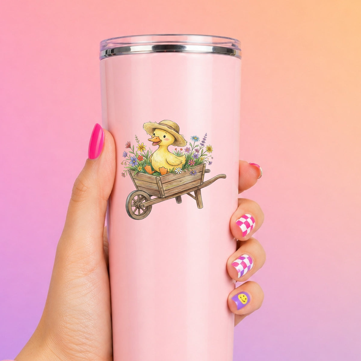 Duckling In Wheelbarrow Of Flowers UV DTF sticker applied to a tall pink tumbler on a pink and orange background
