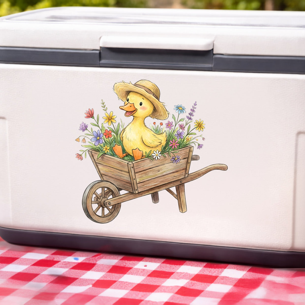Duckling In Wheelbarrow Of Flowers UV DTF sticker applied to a white cooler on a red gingham cloth