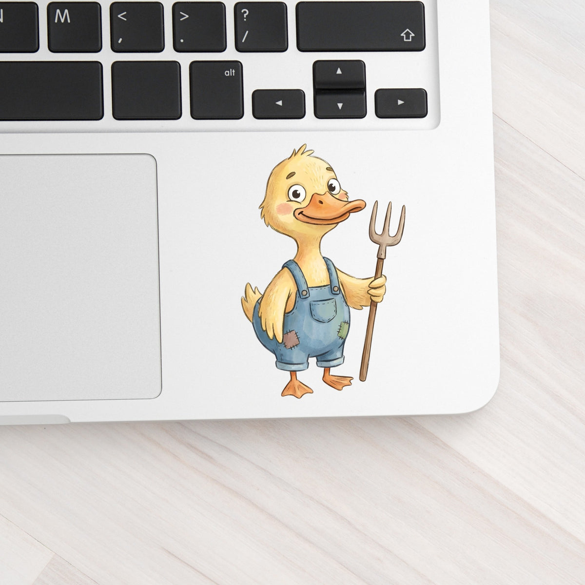 Duck In Overalls Holding Pitchfork UV DTF sticker applied to a silver laptop beside the keyboard