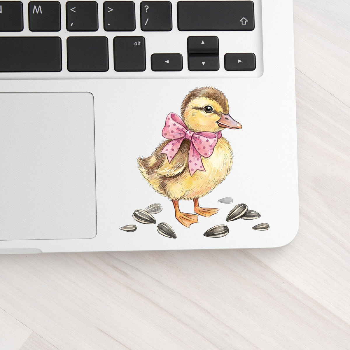 Brown Duckling With Pink Bow UV DTF sticker applied to a silver laptop beside the keyboard