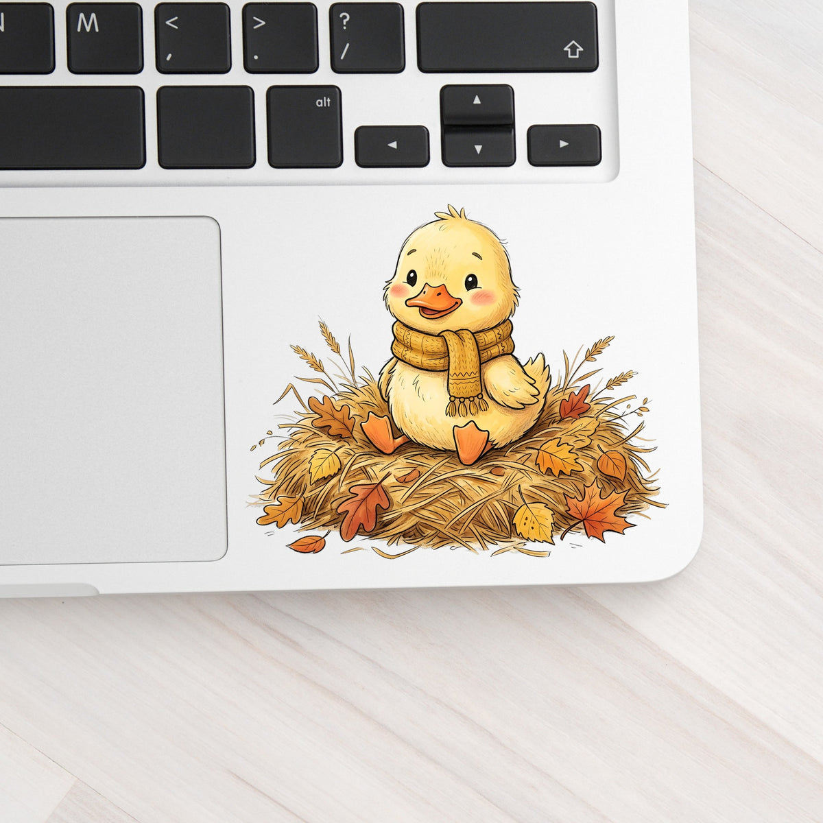 Duckling In Scarf On Hay With Autumn Leaves UV DTF sticker applied to a silver laptop beside the keyboard