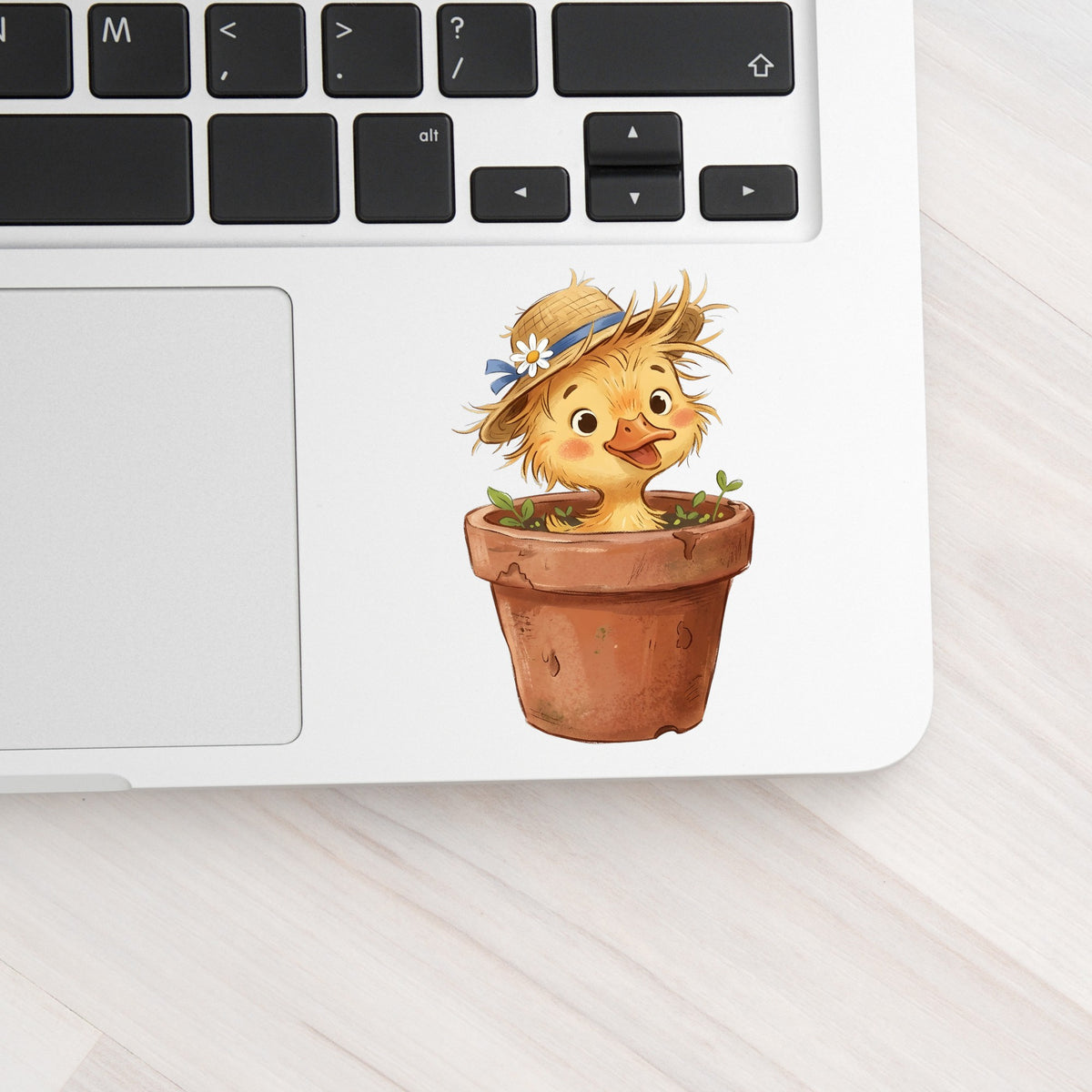 Fluffy Duckling In Flower Pot UV DTF sticker applied to a silver laptop beside the keyboard