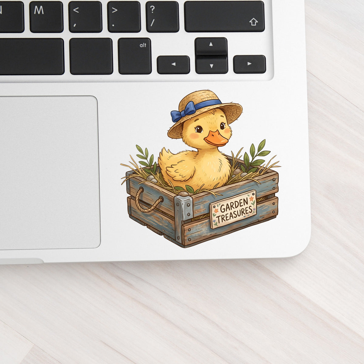 Duckling In Garden Treasures Crate UV DTF sticker applied to a silver laptop beside the keyboard