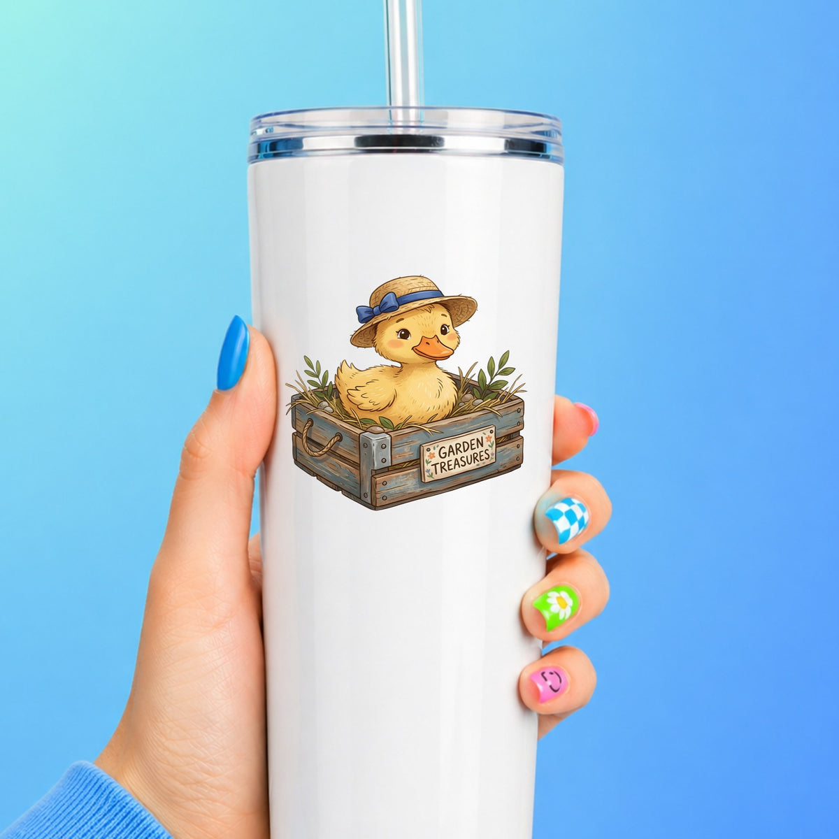 Duckling In Garden Treasures Crate UV DTF sticker applied to a white straw tumbler on a blue background