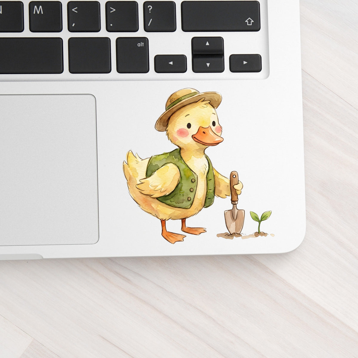 Duck In Green Vest With Garden Trowel UV DTF sticker applied to a silver laptop beside the keyboard
