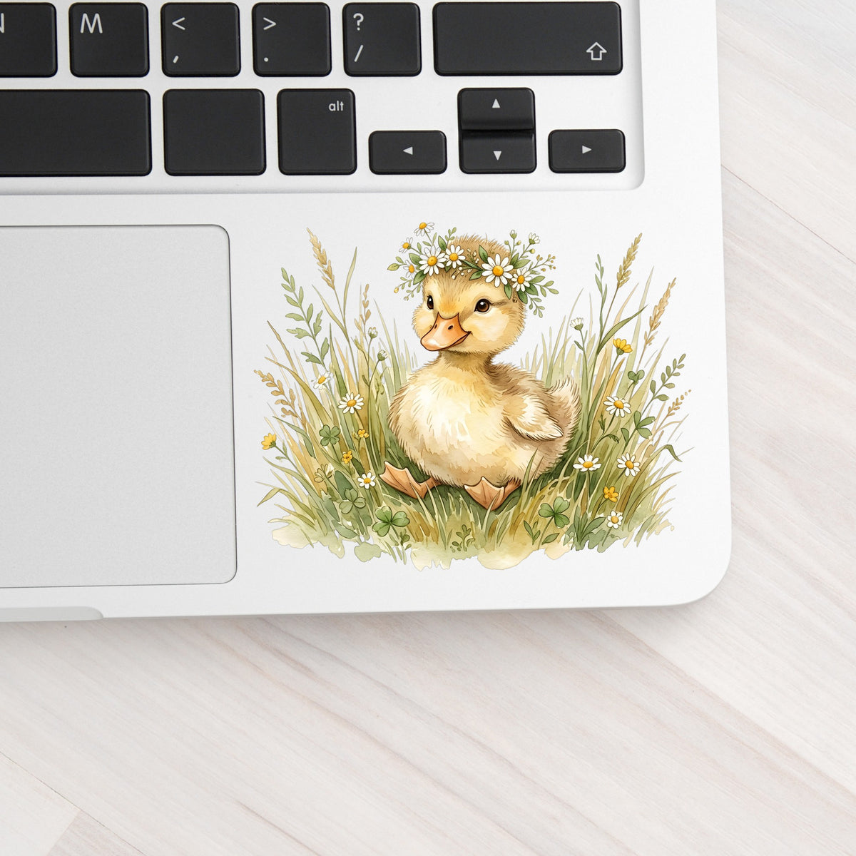 Duckling With Daisy Crown In Grass UV DTF sticker applied to a silver laptop beside the keyboard