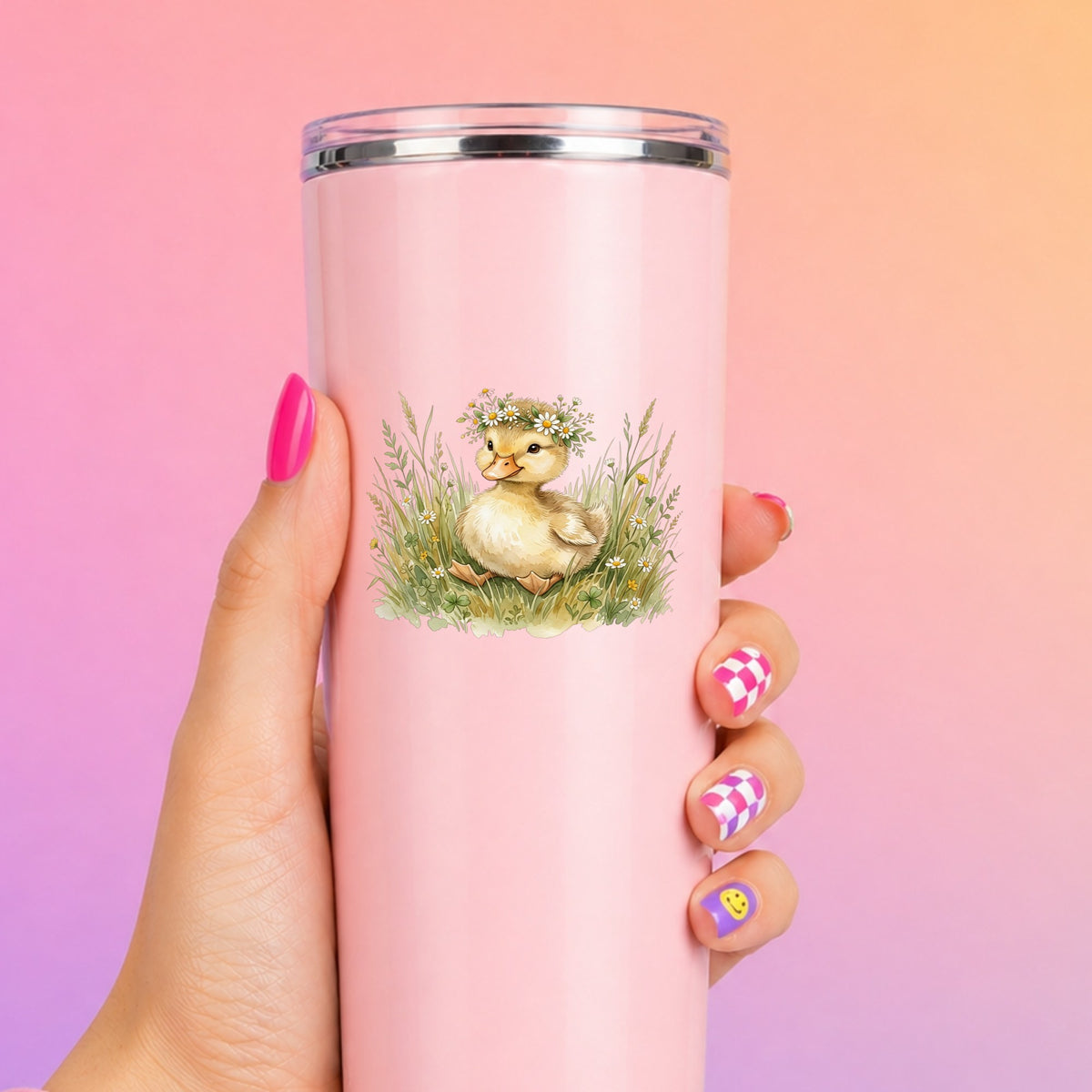 Duckling With Daisy Crown In Grass UV DTF sticker applied to a tall pink tumbler on a pink and orange background