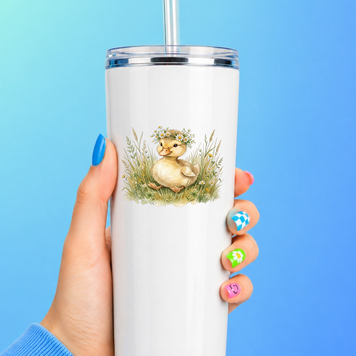 Duckling With Daisy Crown In Grass UV DTF sticker applied to a white straw tumbler on a blue background