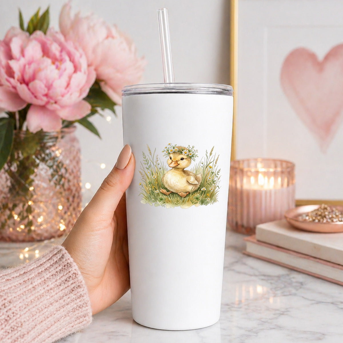 Duckling With Daisy Crown In Grass UV DTF sticker applied to a white straw tumbler beside pink peonies