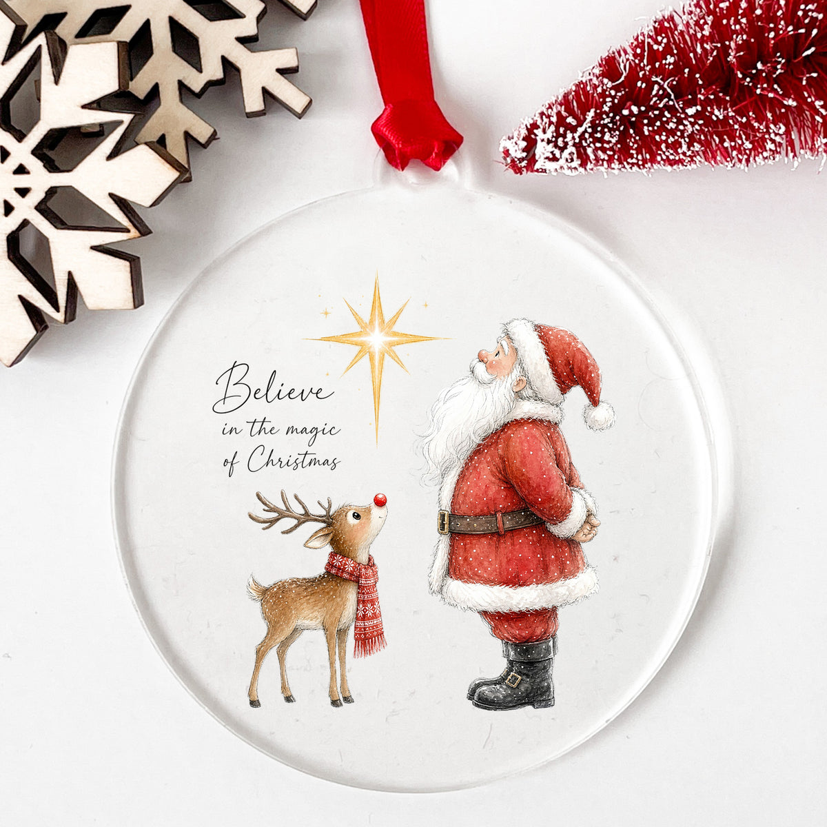 Believe Santa And Reindeer UV DTF sticker applied to a clear round acrylic ornament with a red ribbon