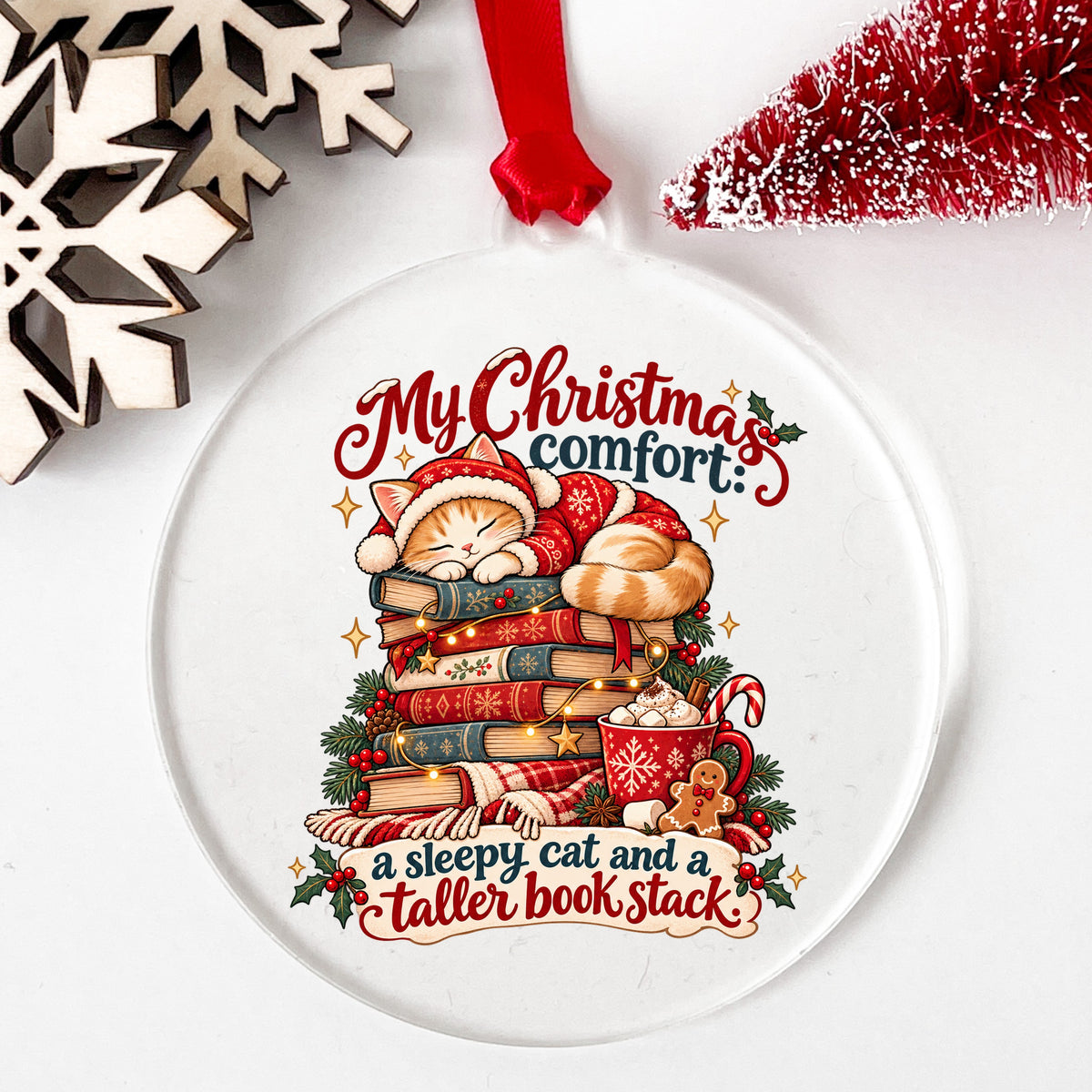 Sleepy Christmas Cat On Book Stack UV DTF sticker applied to a clear round acrylic ornament with a red ribbon