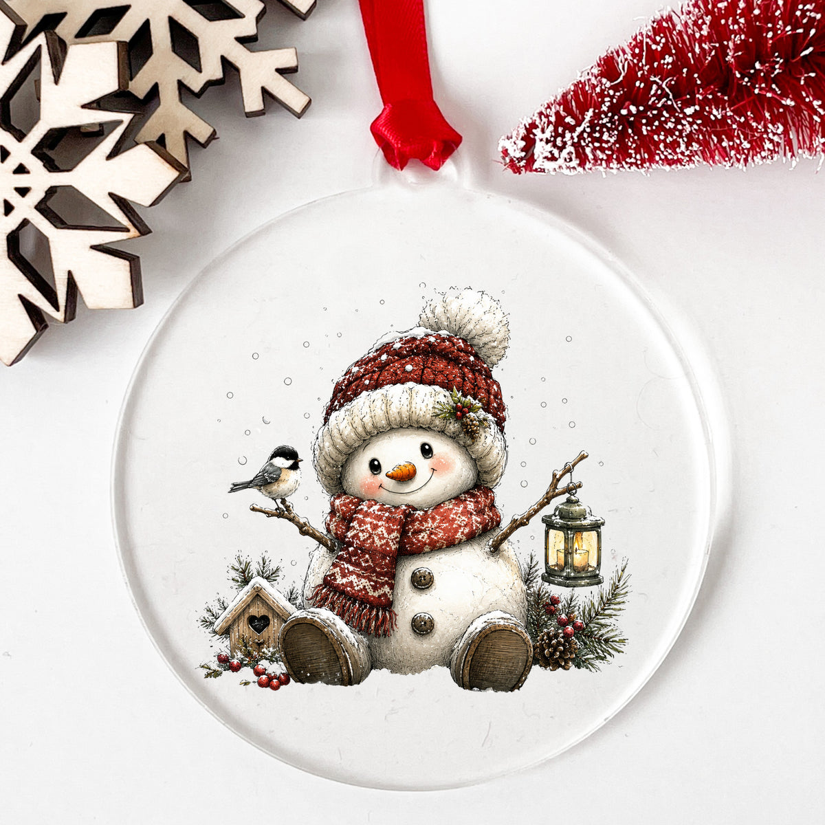 Chickadee Snowman With Birdhouse UV DTF sticker applied to a clear round acrylic ornament with a red ribbon