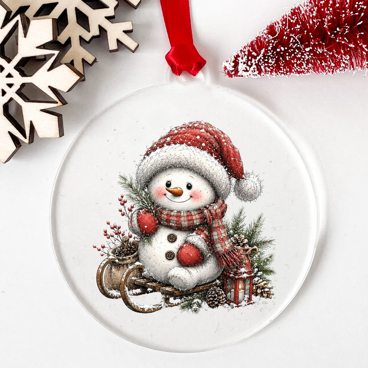 Snowman On Wooden Sled UV DTF sticker applied to a clear round acrylic ornament with a red ribbon
