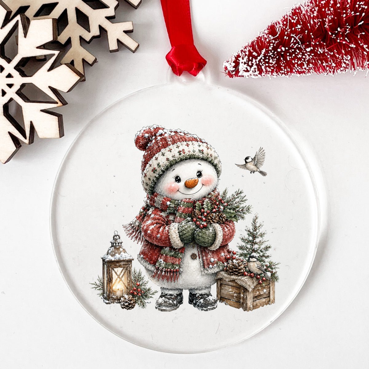 Snowman In Red Sweater Holding Holly UV DTF sticker applied to a clear round acrylic ornament with a red ribbon