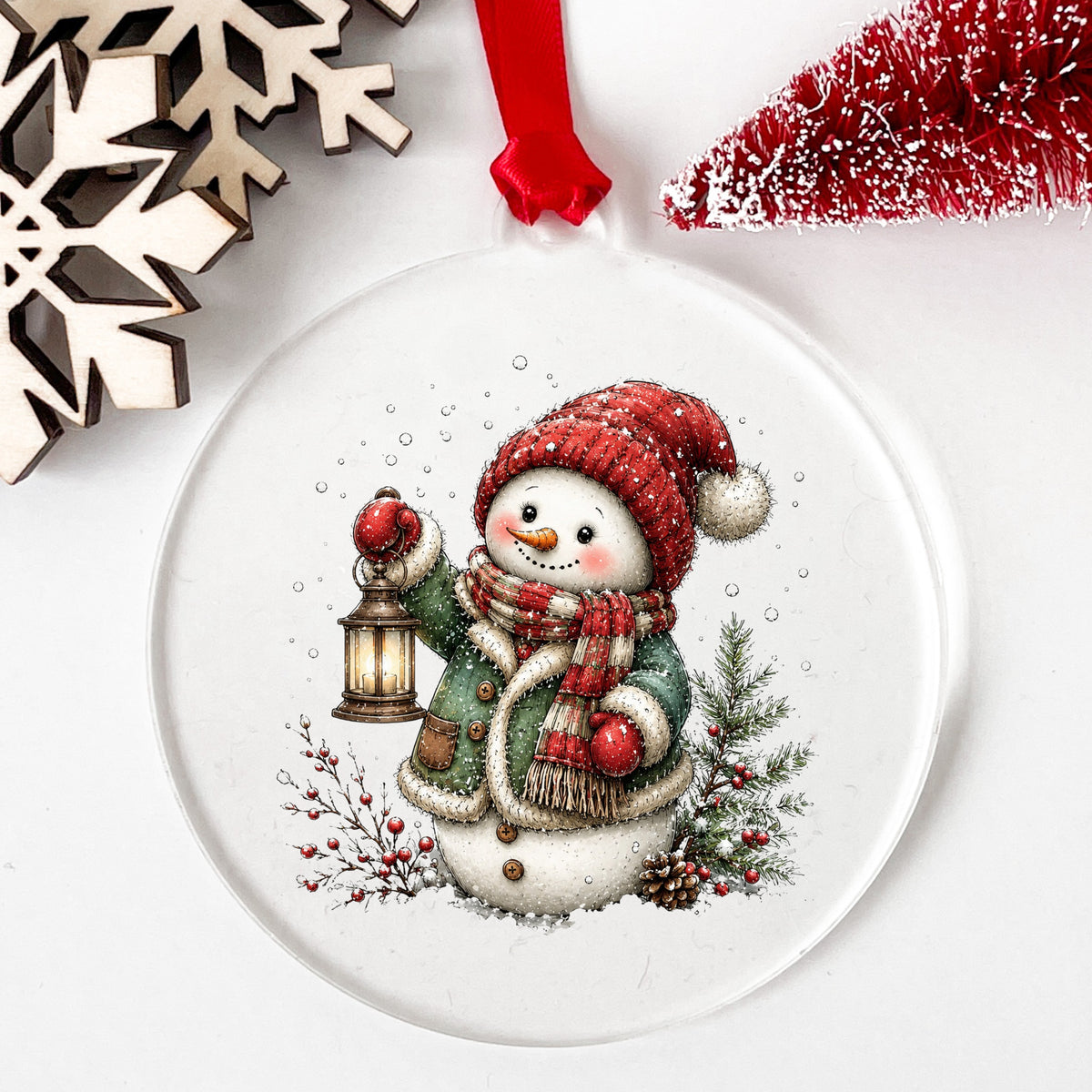 Green Coat Snowman Holding Lantern UV DTF sticker applied to a clear round acrylic ornament with a red ribbon