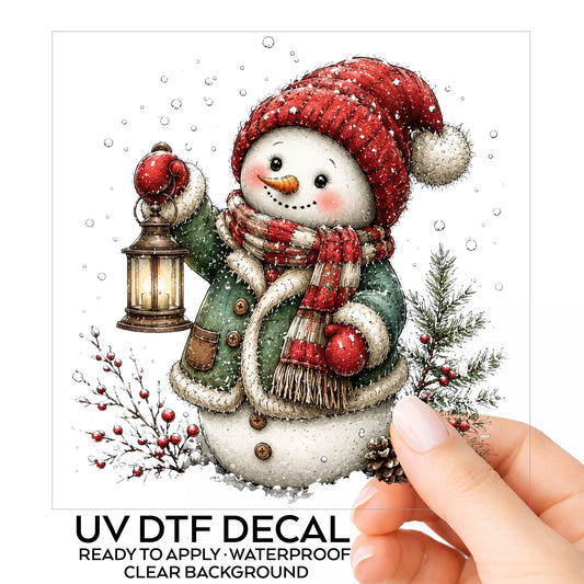 Green Coat Snowman Holding Lantern UV DTF sticker on its backing card, held in hand