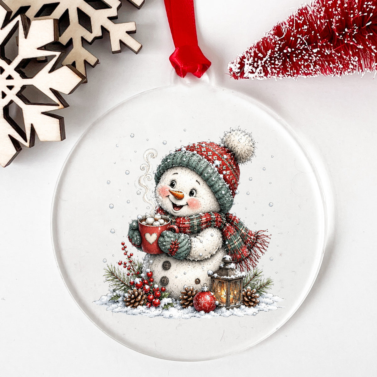 Hot Cocoa Snowman With Heart Mug UV DTF sticker applied to a clear round acrylic ornament with a red ribbon