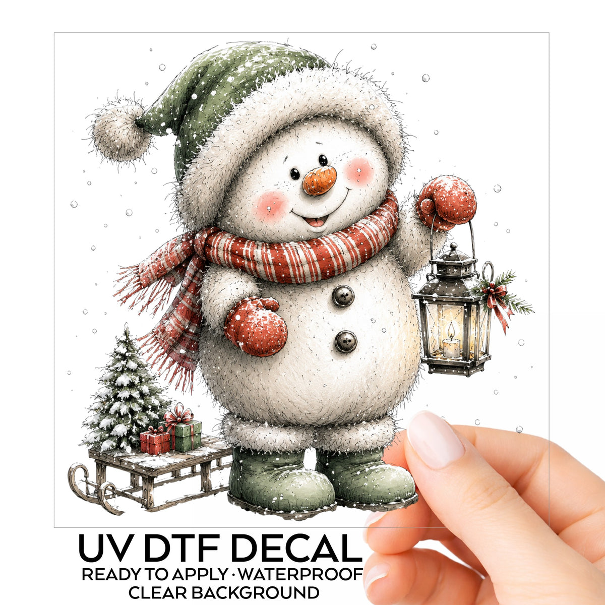 Green Hat Snowman With Sled And Gifts UV DTF sticker on its backing card, held in hand