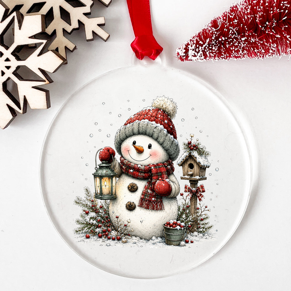 Snowman With Birdhouse And Berry Bucket UV DTF sticker applied to a clear round acrylic ornament with a red ribbon