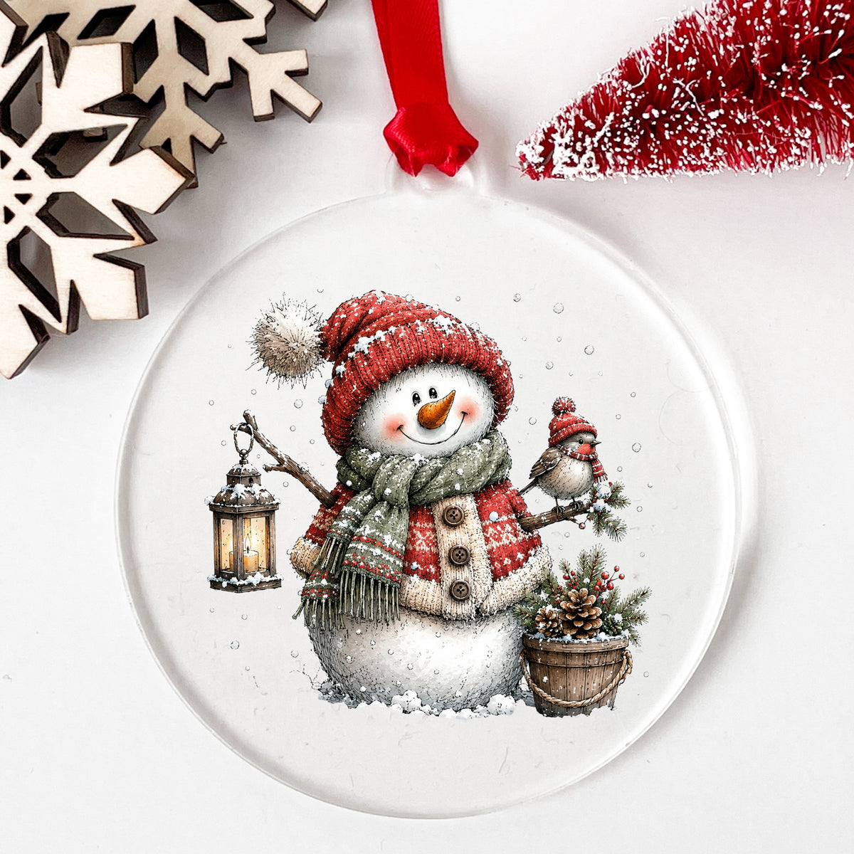 Fair Isle Sweater Snowman With Bird UV DTF sticker applied to a clear round acrylic ornament with a red ribbon