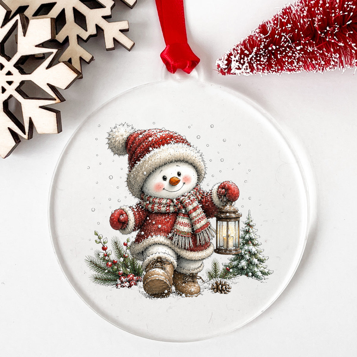 Snowman In Red Knit Coat With Lantern UV DTF sticker applied to a clear round acrylic ornament with a red ribbon
