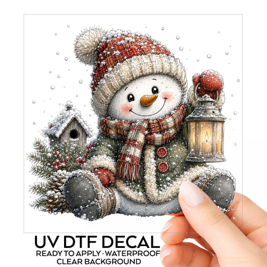 Sitting Snowman In Green Coat With Birdhouse UV DTF sticker on its backing card, held in hand