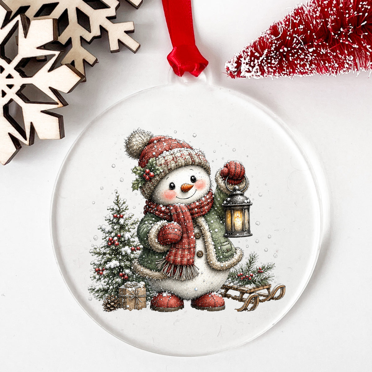 Snowman With Holly Hat And Christmas Tree UV DTF sticker applied to a clear round acrylic ornament with a red ribbon