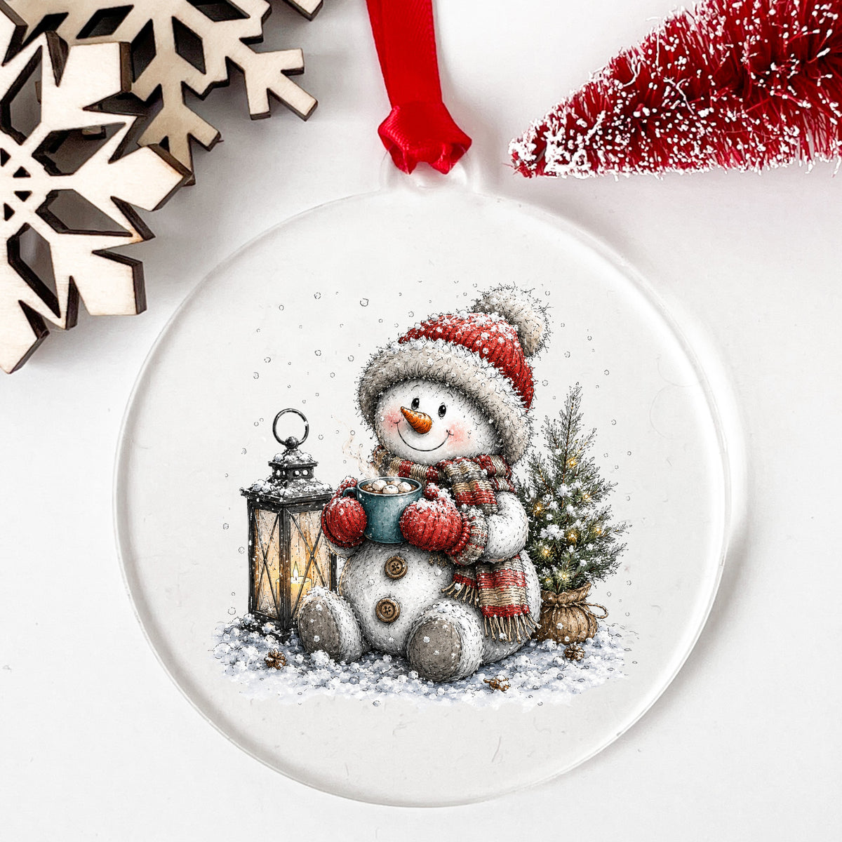 Snowman Sipping Cocoa By Lantern UV DTF sticker applied to a clear round acrylic ornament with a red ribbon