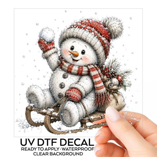 Snowball Snowman On Sled UV DTF sticker on its backing card, held in hand