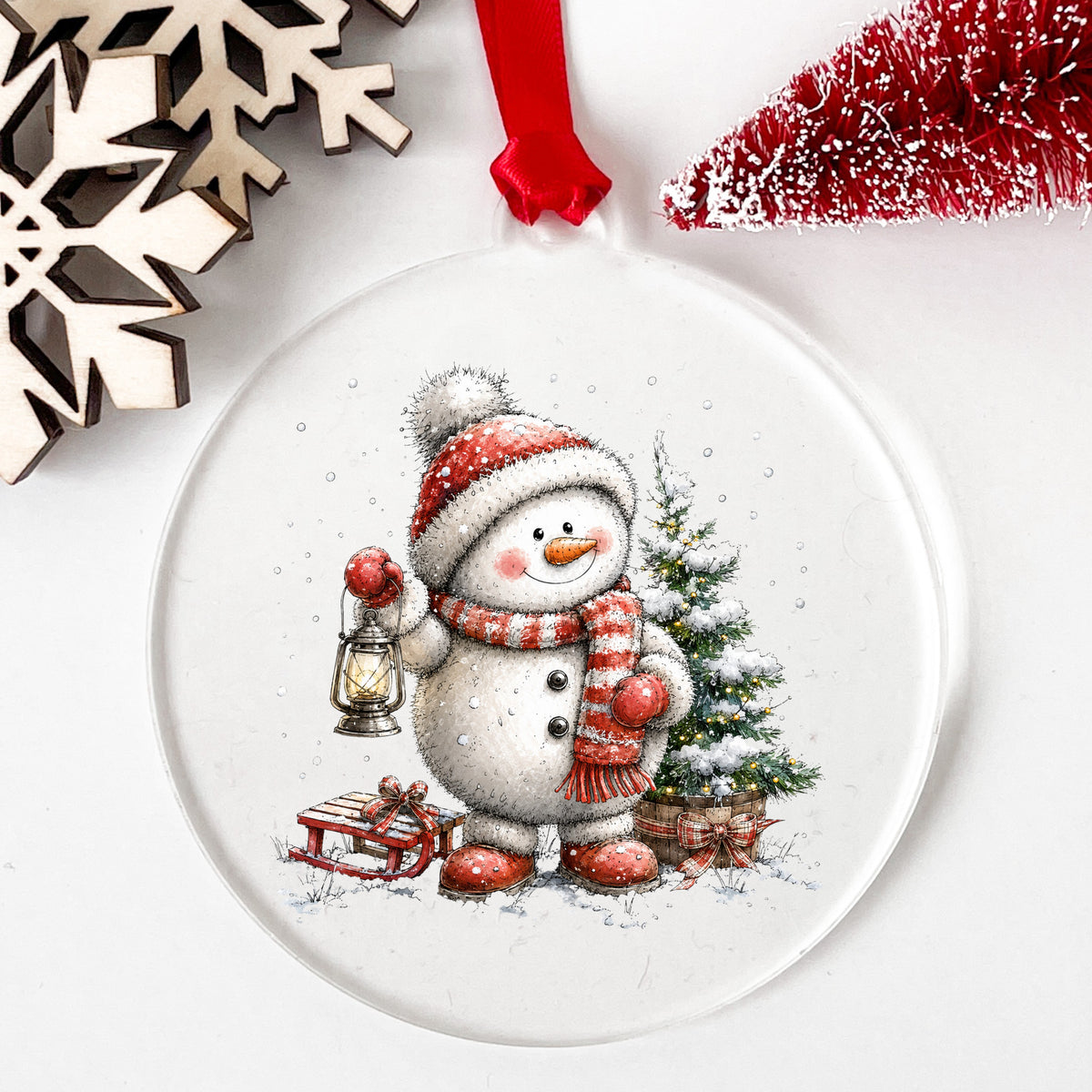 Striped Scarf Snowman With Lantern UV DTF sticker applied to a clear round acrylic ornament with a red ribbon