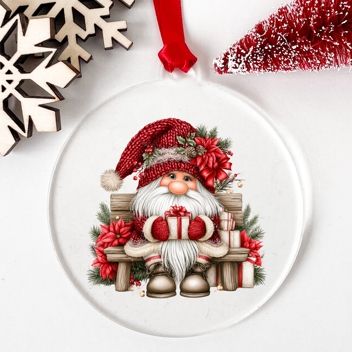 Gnome Sitting On Bench With Poinsettias UV DTF sticker applied to a clear round acrylic ornament with a red ribbon