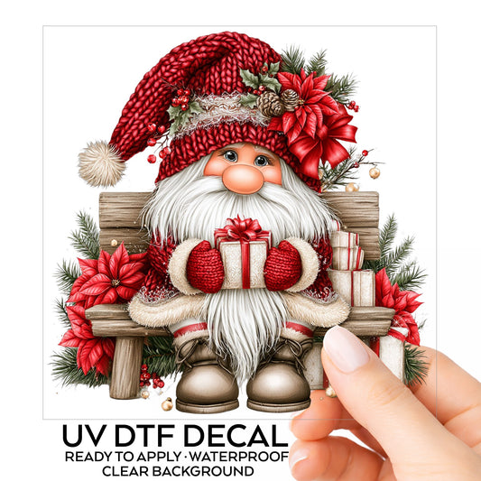 Gnome Sitting On Bench With Poinsettias UV DTF sticker on its backing card, held in hand