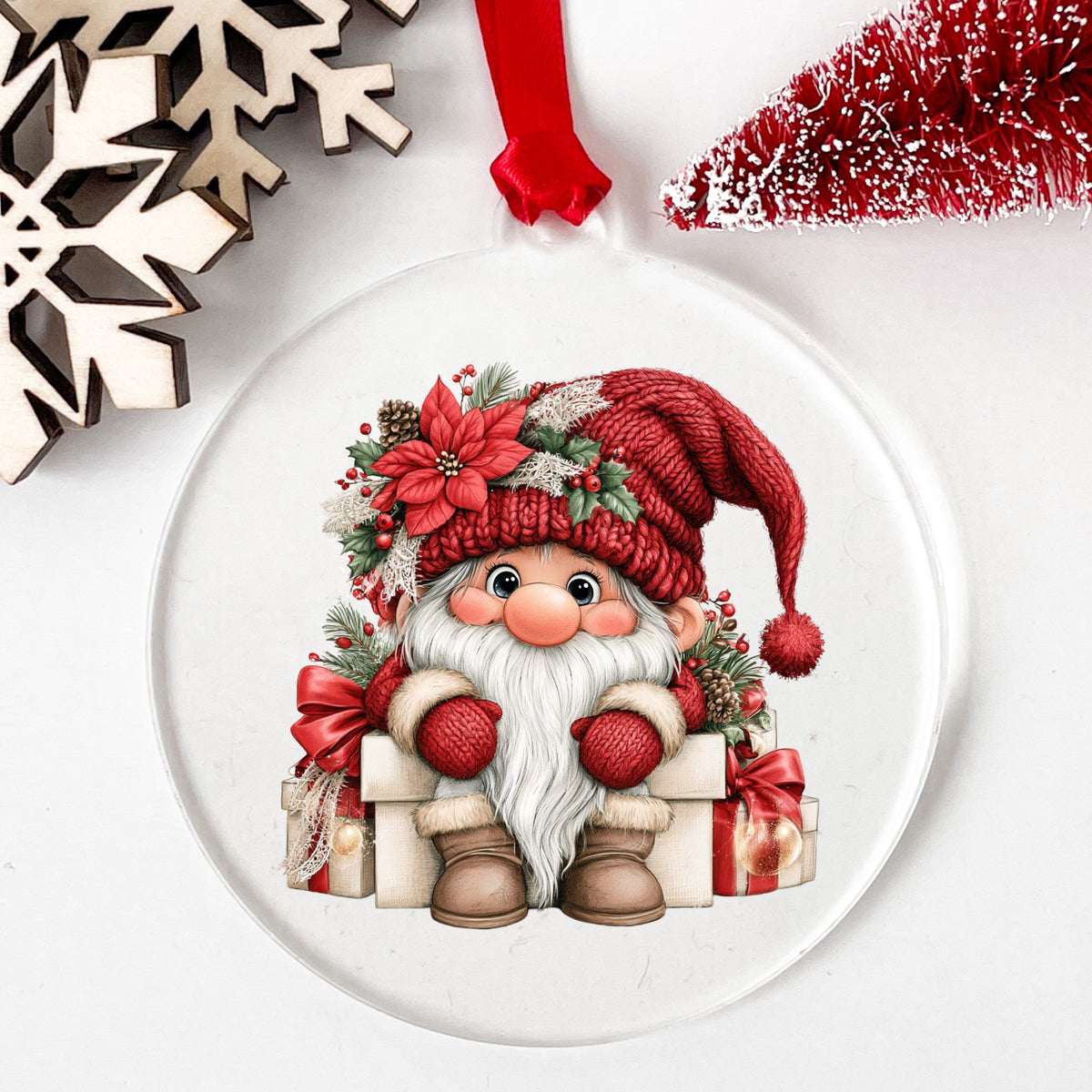 Gnome Sitting On Gift Boxes UV DTF sticker applied to a clear round acrylic ornament with a red ribbon