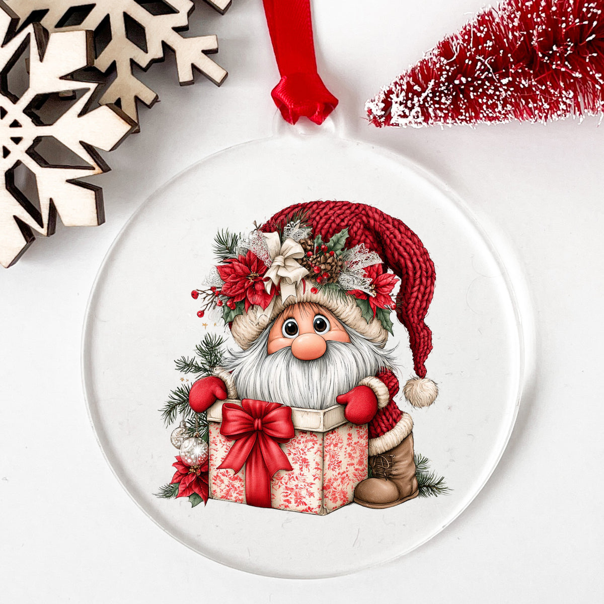 Gnome Peeking From Gift Box UV DTF sticker applied to a clear round acrylic ornament with a red ribbon