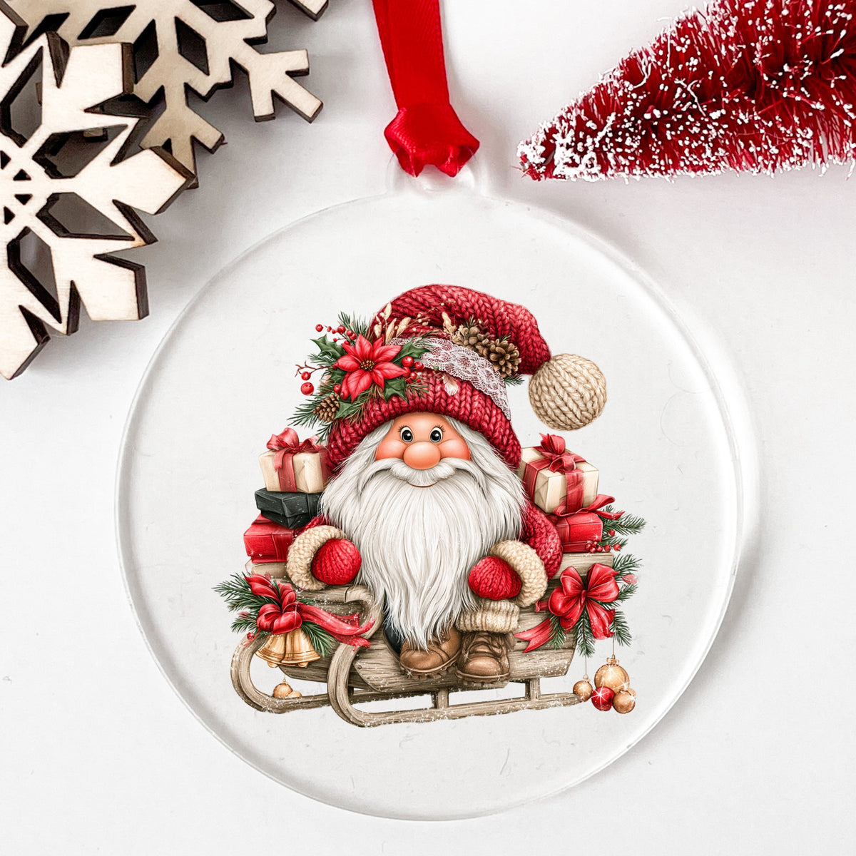 Gnome Riding Wooden Sleigh With Gifts UV DTF sticker applied to a clear round acrylic ornament with a red ribbon
