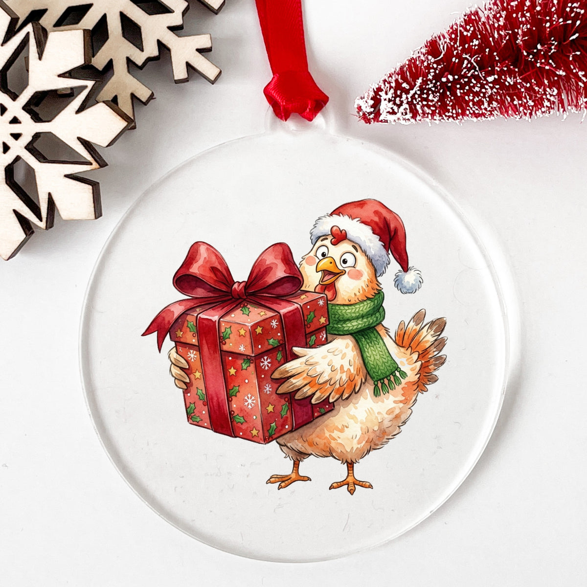 Chicken Carrying Red Christmas Gift UV DTF sticker applied to a clear round acrylic ornament with a red ribbon