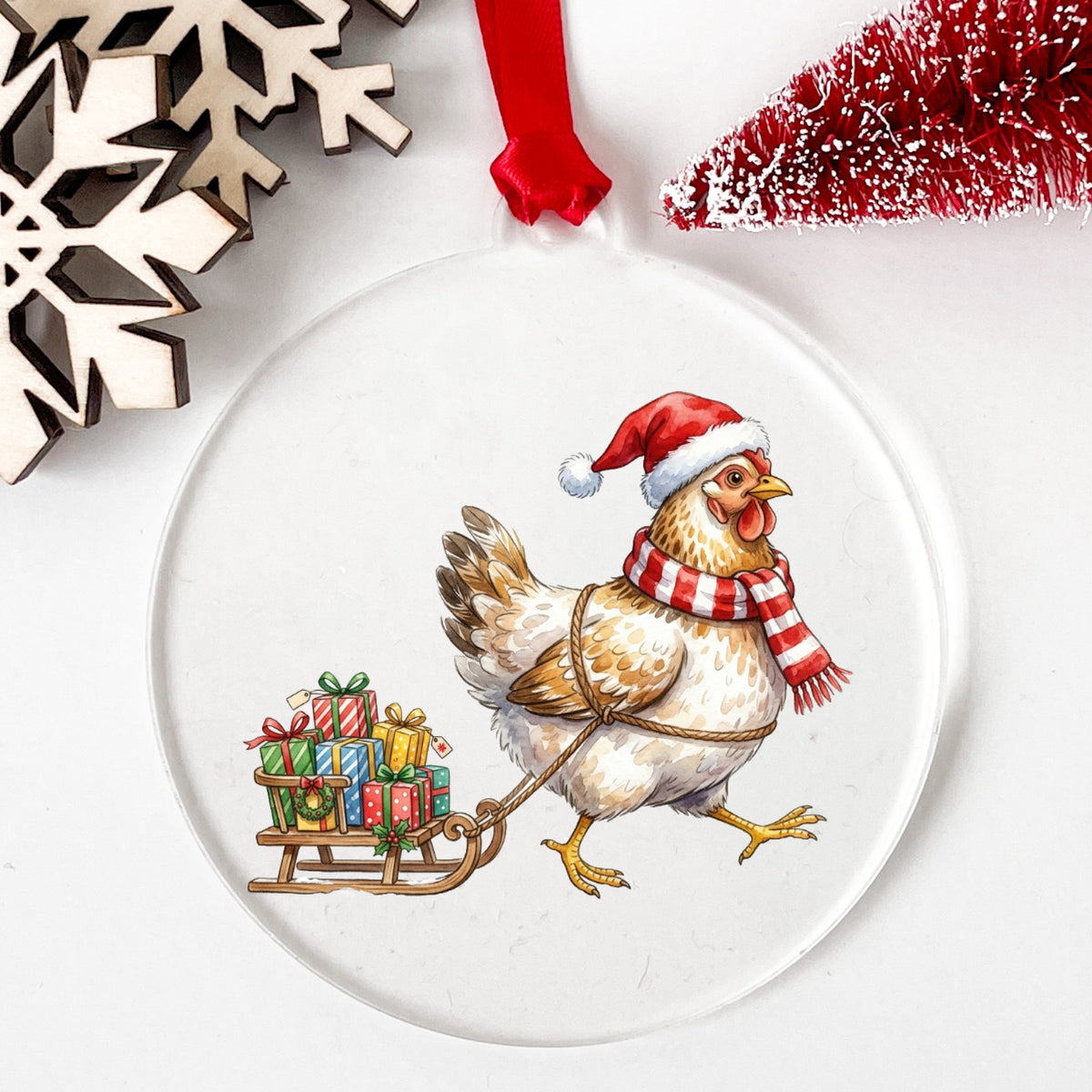 Chicken Pulling Sled Of Presents UV DTF sticker applied to a clear round acrylic ornament with a red ribbon
