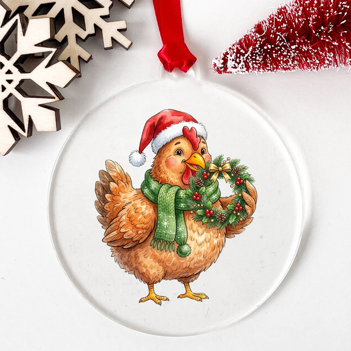 Hen Holding Holly Wreath UV DTF sticker applied to a clear round acrylic ornament with a red ribbon