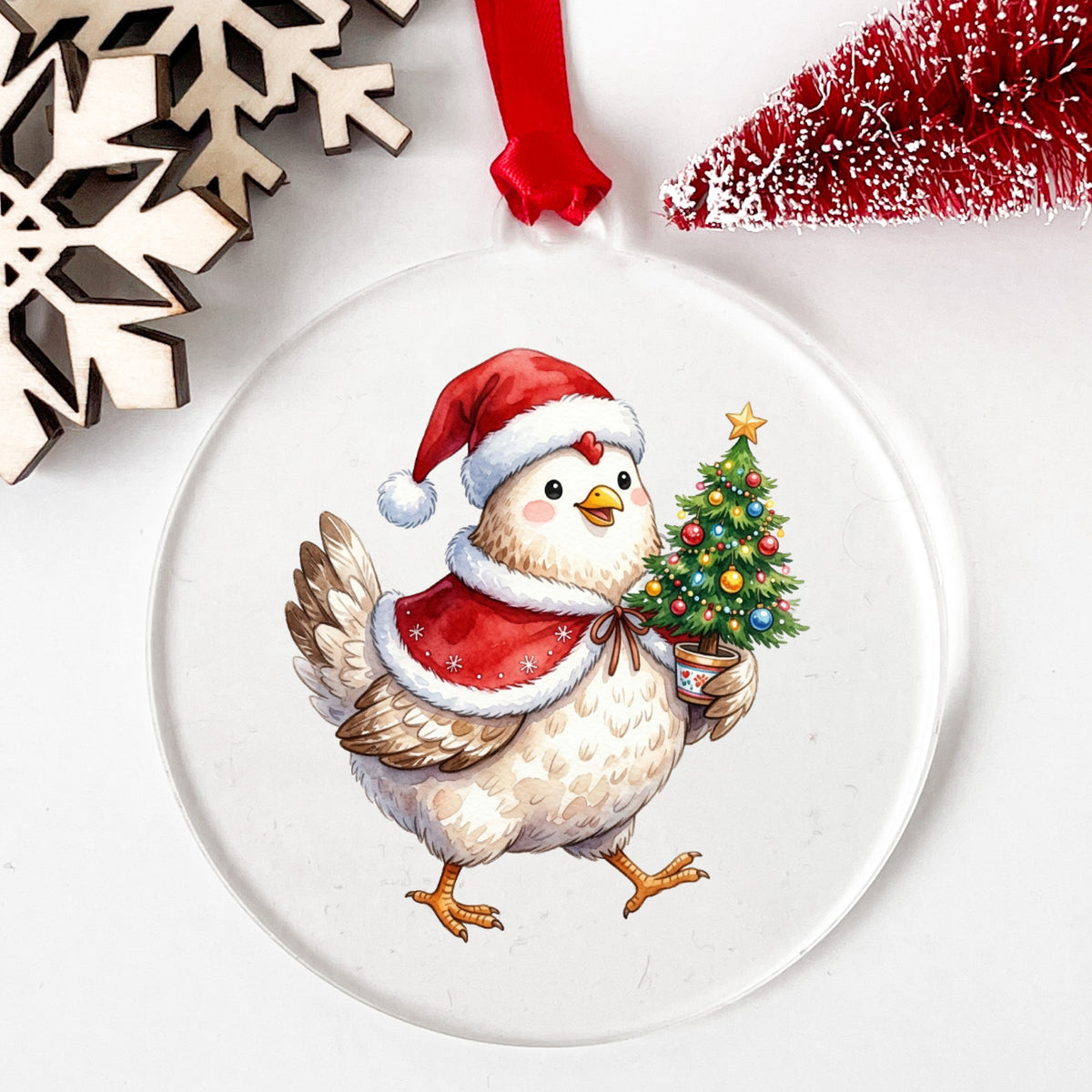 Chicken Carrying Small Christmas Tree UV DTF sticker applied to a clear round acrylic ornament with a red ribbon
