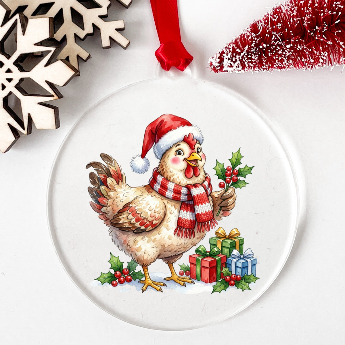 Hen With Holly And Presents UV DTF sticker applied to a clear round acrylic ornament with a red ribbon