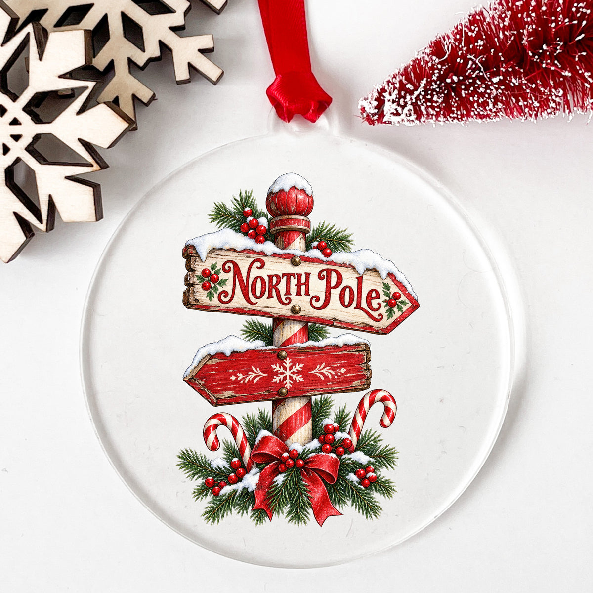 North Pole Sign UV DTF sticker applied to a clear round acrylic ornament with a red ribbon
