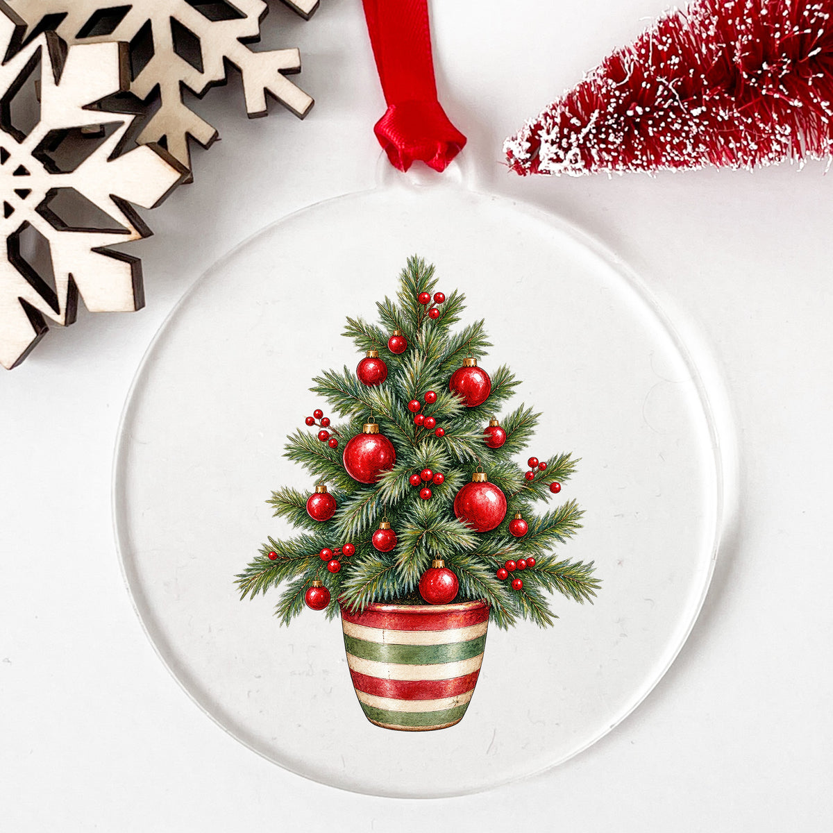 Potted Christmas Tree With Red Ornaments UV DTF sticker applied to a clear round acrylic ornament with a red ribbon