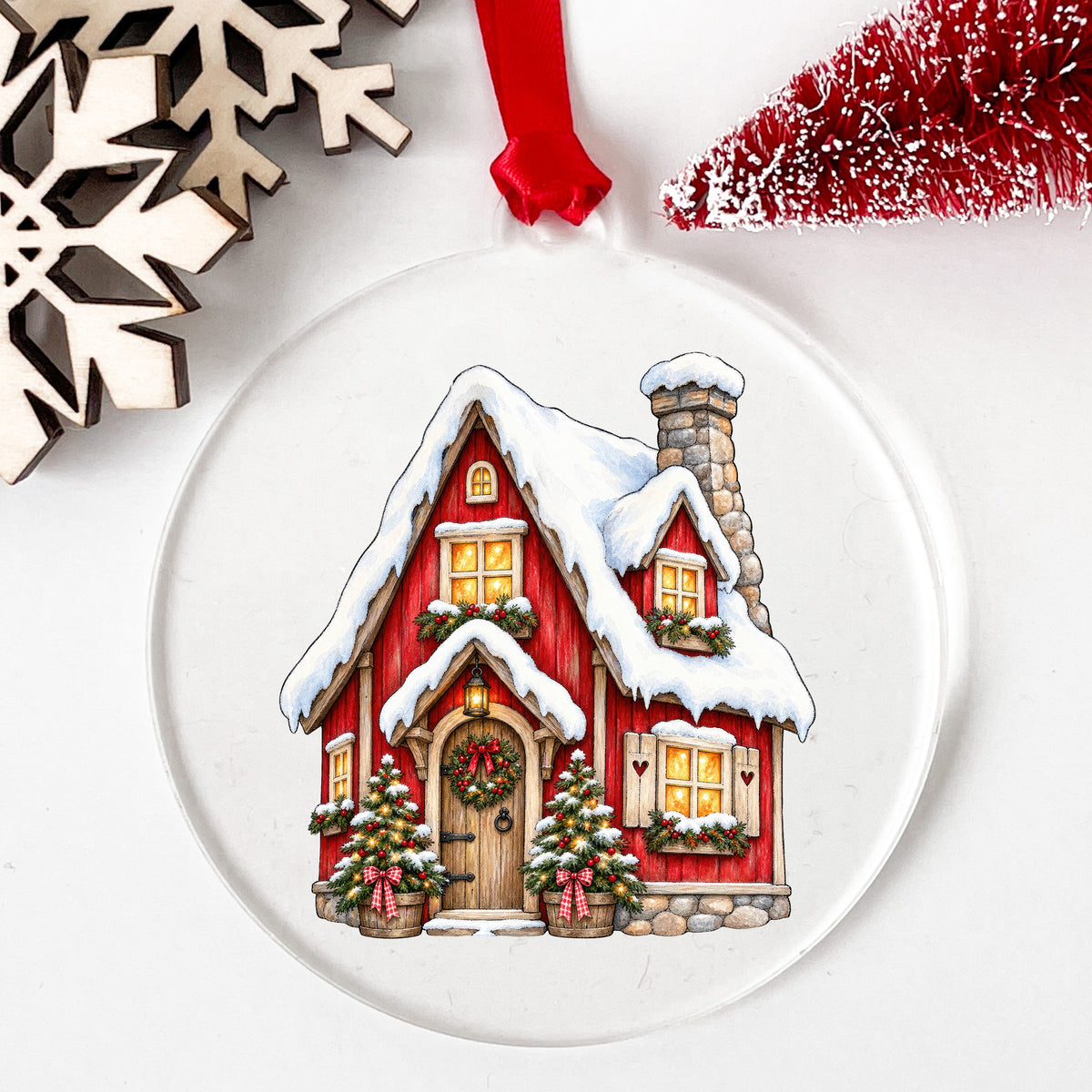 Red Christmas Cottage In Snow UV DTF sticker applied to a clear round acrylic ornament with a red ribbon