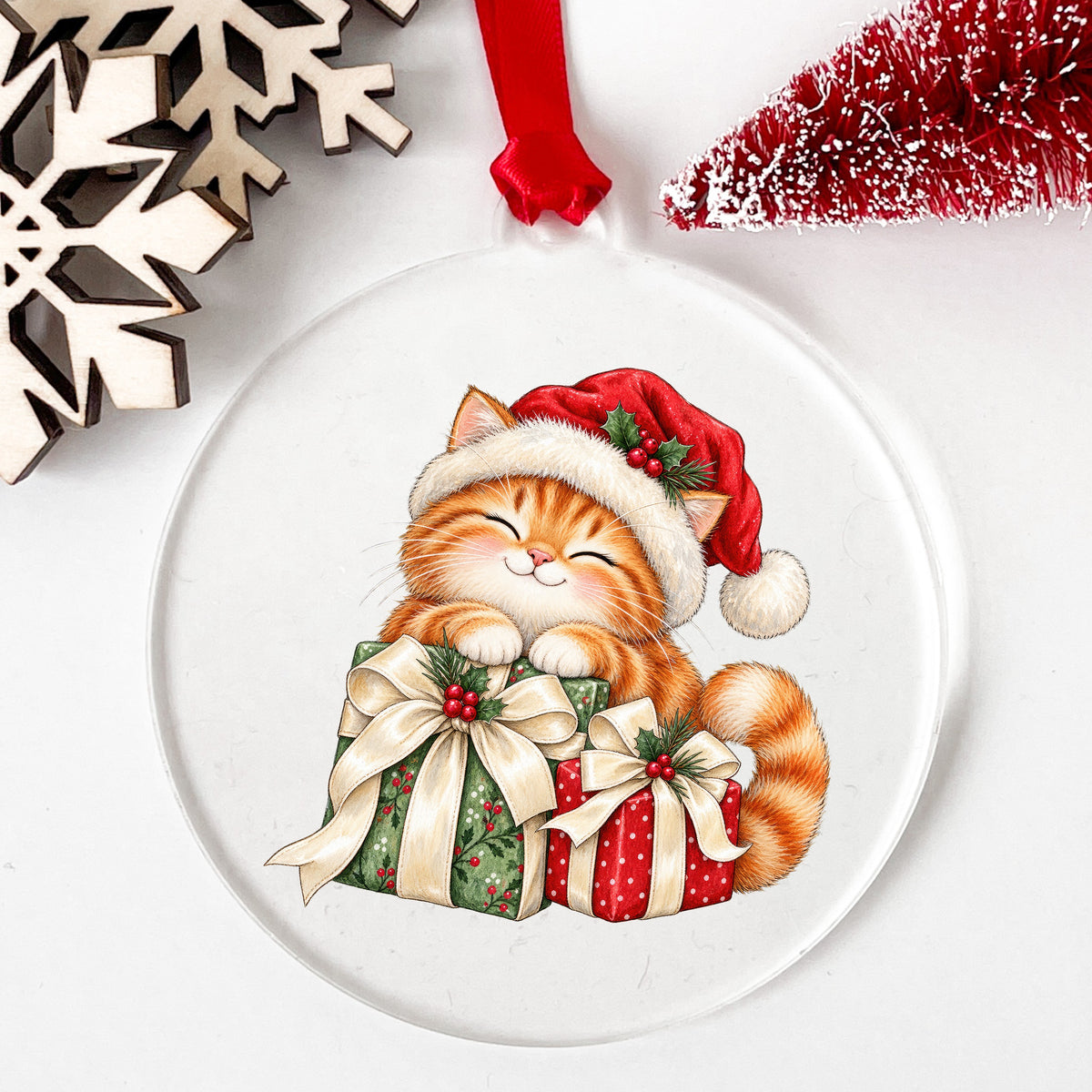 Orange Kitten With Christmas Gifts UV DTF sticker applied to a clear round acrylic ornament with a red ribbon
