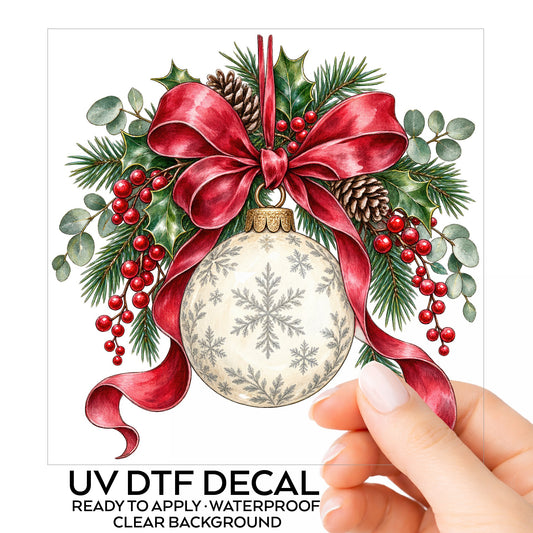 Snowflake Ornament With Red Bow UV DTF sticker on its backing card, held in hand