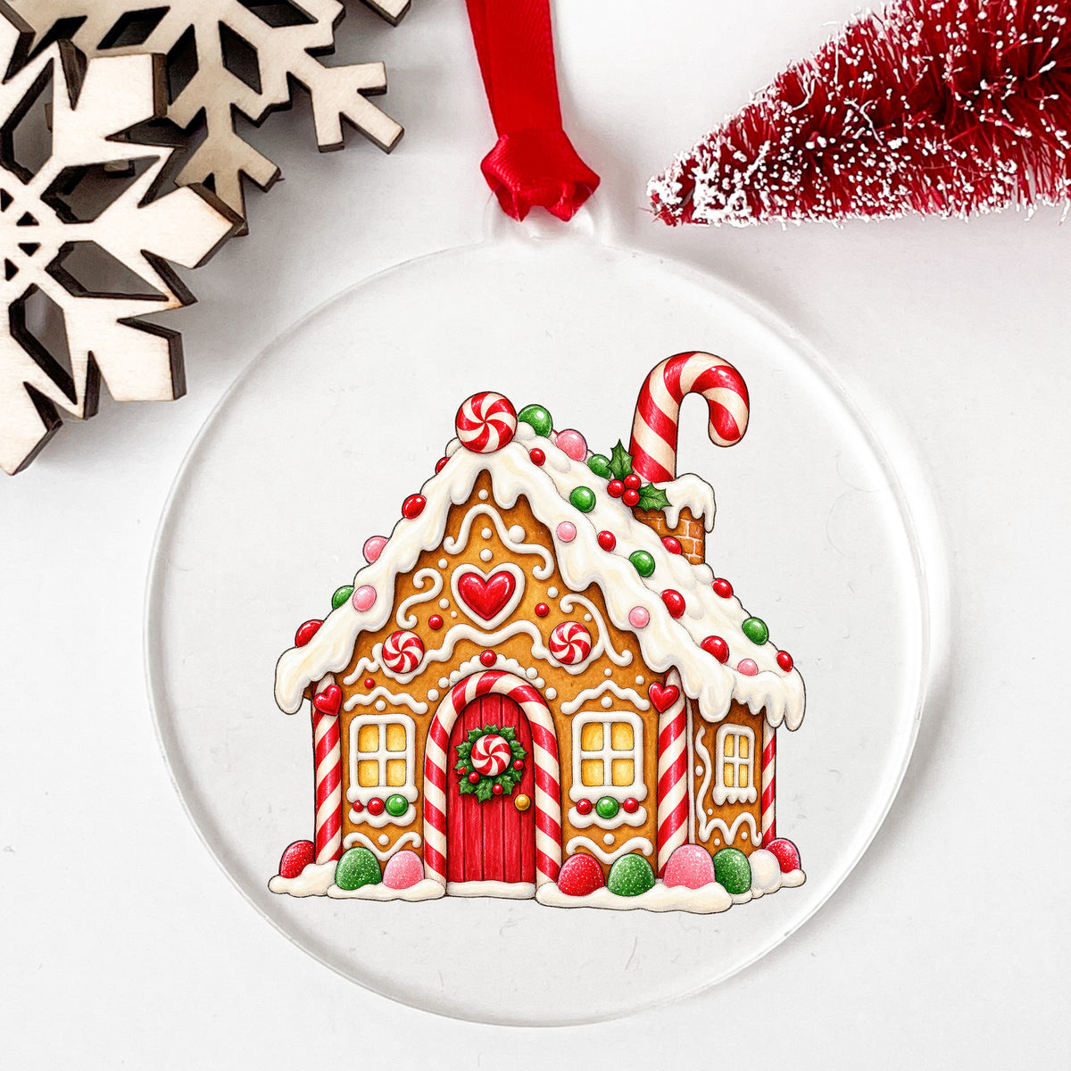 Gingerbread House With Candy UV DTF sticker applied to a clear round acrylic ornament with a red ribbon